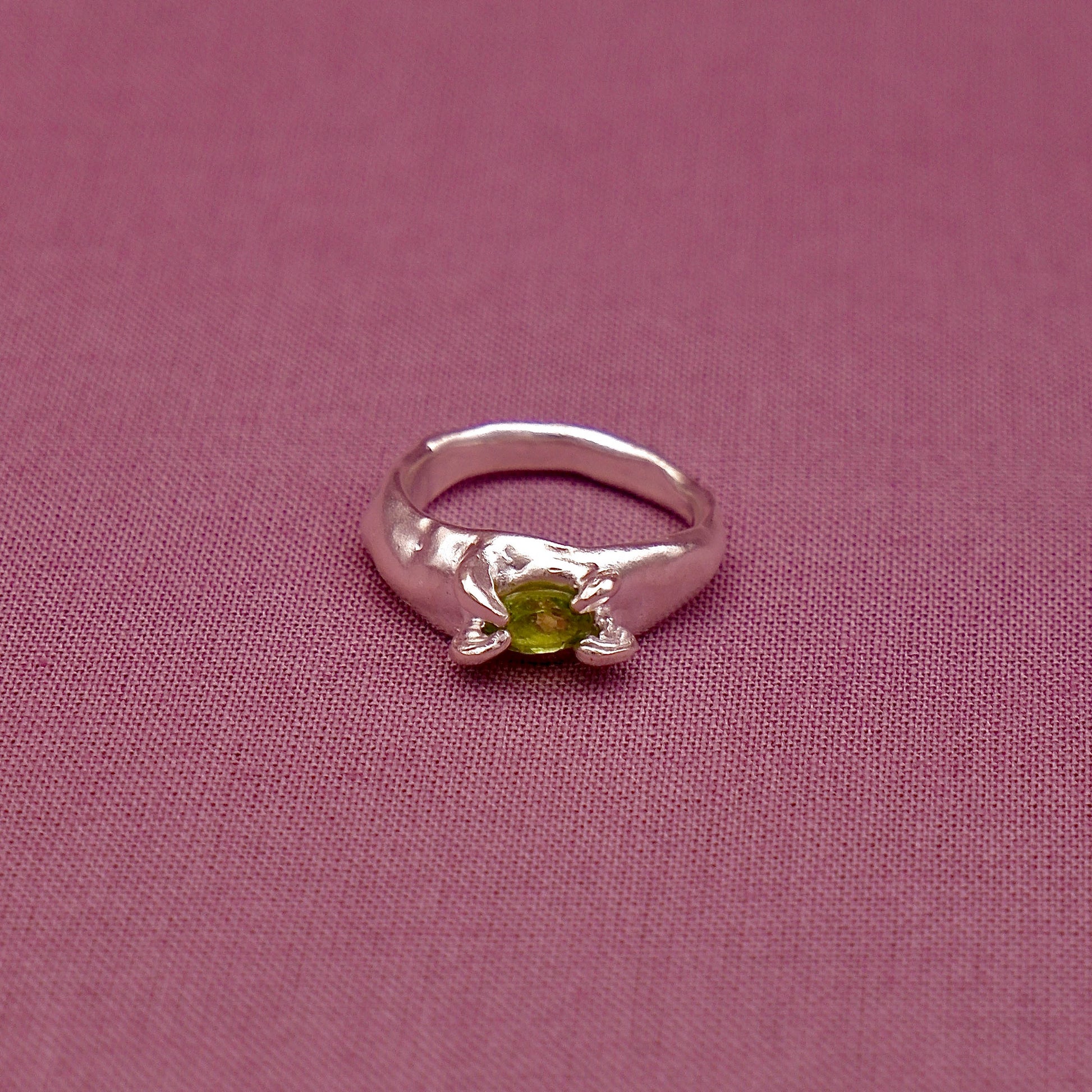 Silver ring with a green gemstone on a pink fabric background
