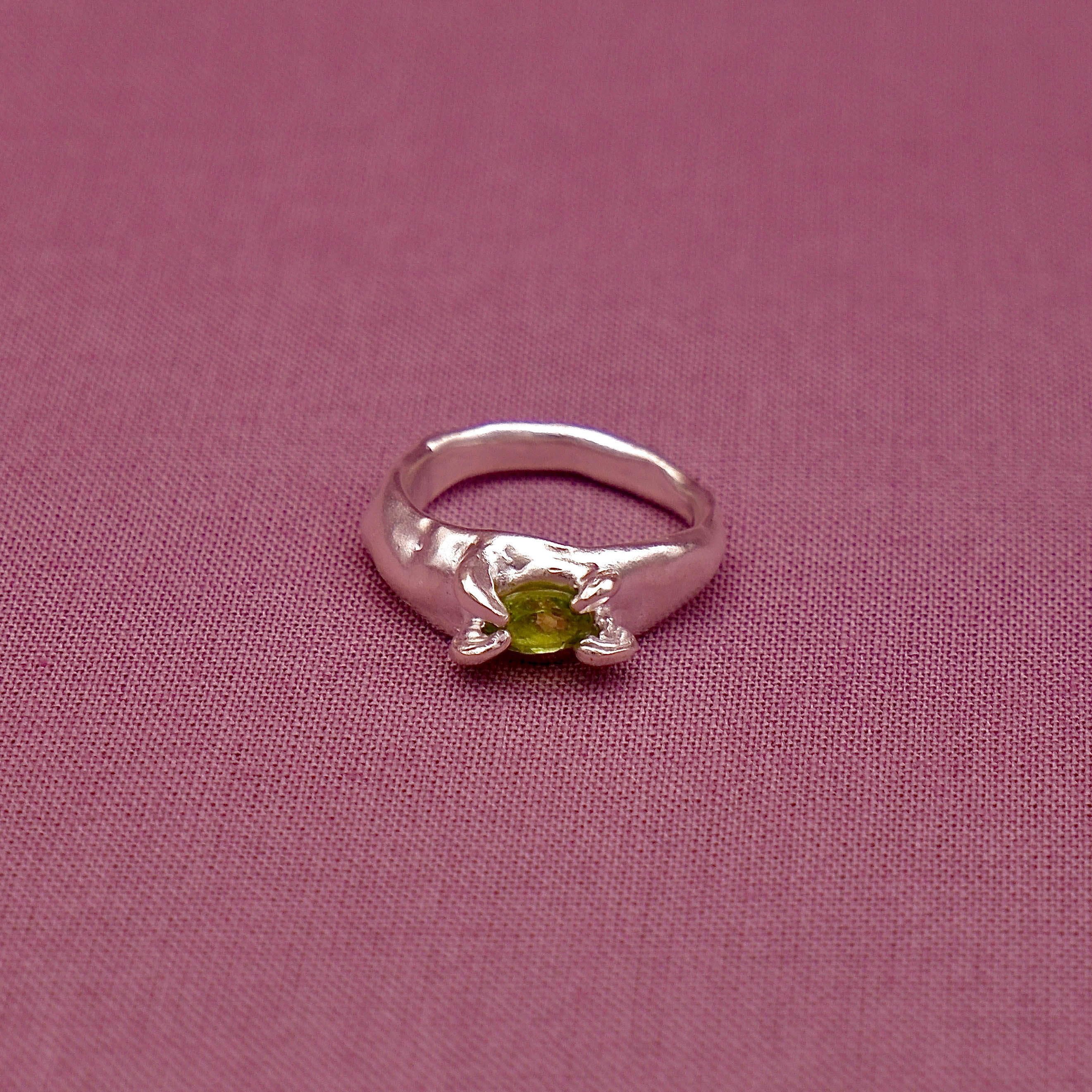Silver ring with a green gemstone on a pink fabric background